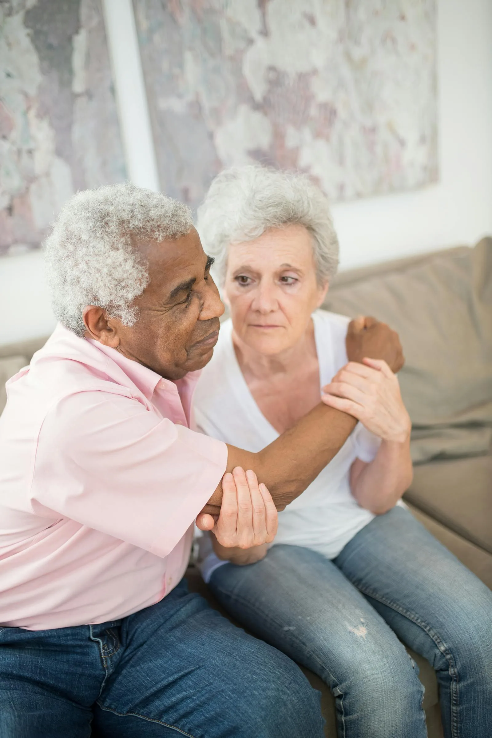 A husband gently holds his wife's hand as they sit together on a couch.