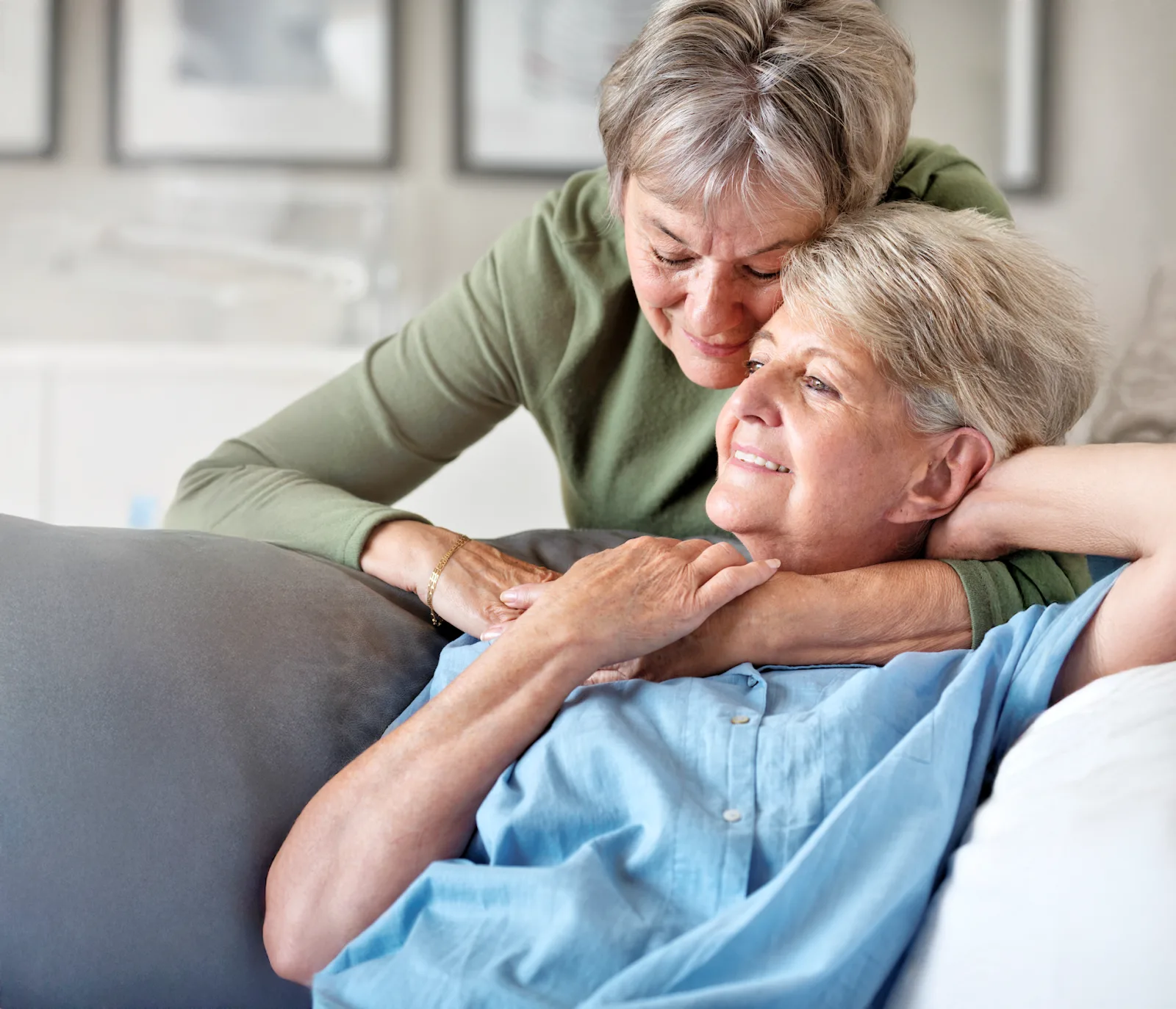 Two older women holding each other on a couch, smiling.