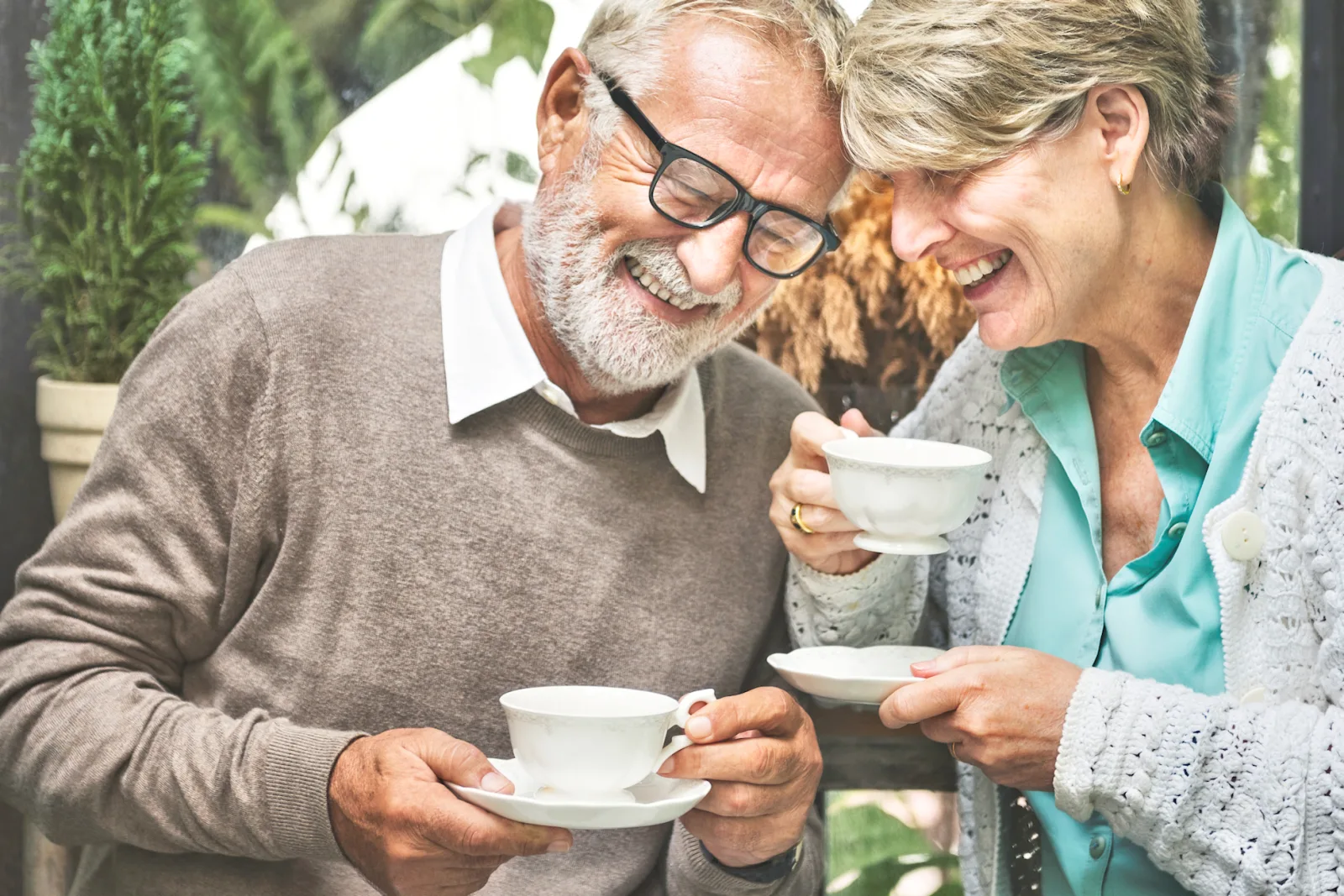 An older couple sharing tea, leaning together and laughing.